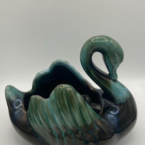 May include: A ceramic swan-shaped bowl in teal, green, and black. The swan has a curved neck and a wide, open bowl. The glossy finish gives it a vintage look, suitable for home decor.