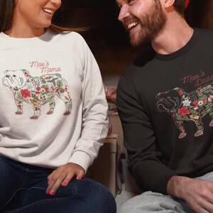 Peut inclure: Deux sweatshirts, un gris clair et un noir, avec un motif de bouledogue floral. Le texte "Max's Mama" et "Max's Daddy" est en rouge. Le motif du bouledogue comprend des &eacute;l&eacute;ments floraux rouges, blancs et verts.
