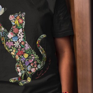 May include: Black t-shirt featuring a floral cat design with a butterfly. The cat silhouette is filled with colorful flowers and greenery. The words "Love is..." are written in cursive on the shirt.