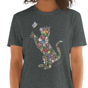 May include: Dark gray t-shirt featuring a floral cat design reaching for a butterfly. The cat silhouette is filled with colorful flowers and foliage. The words "Love it" are written in cursive.