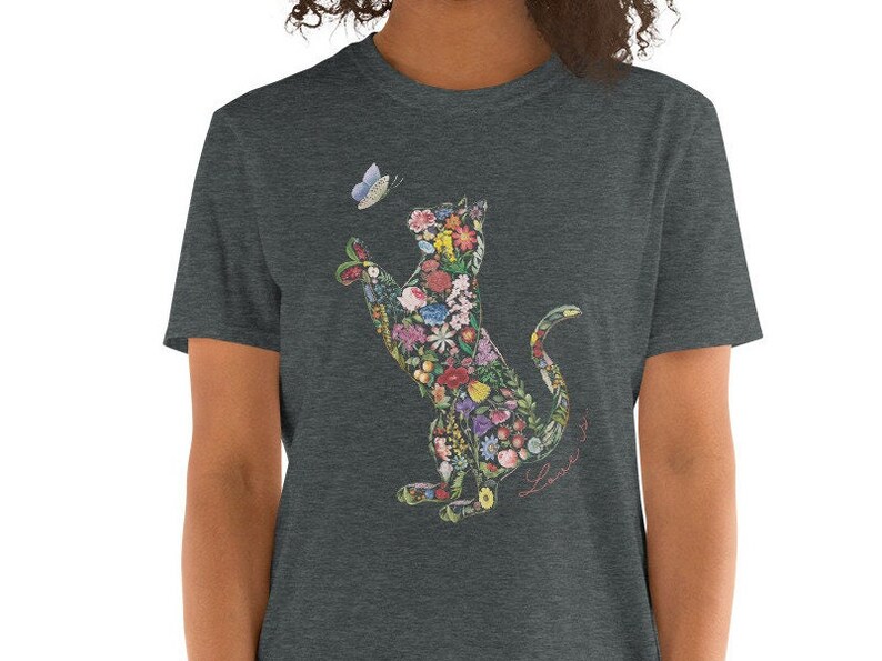 May include: Dark gray t-shirt featuring a floral cat design reaching for a butterfly. The cat silhouette is filled with colorful flowers and foliage. The words "Love it" are written in cursive.