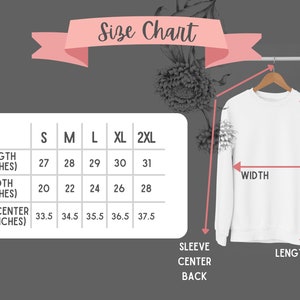 Peut inclure: Un sweat-shirt blanc est suspendu &agrave; un cintre en bois, avec un tableau des tailles affich&eacute; &agrave; gauche. Le tableau indique les mesures de longueur, de largeur et de dos de manche en pouces pour les tailles S, M, L, XL et 2XL. Le texte "Size Chart" est en haut.