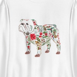 Peut inclure: Sweat-shirt blanc avec une illustration &agrave; l'aquarelle d'un bouledogue orn&eacute; de feuillage de No&euml;l. Le bouledogue est orn&eacute; de poinsettias rouges, de feuilles vertes et de pommes de pin, cr&eacute;ant un design de vacances festif.