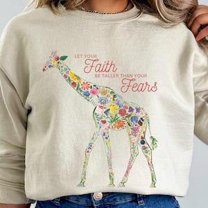 May include: A beige sweatshirt with a floral giraffe design and the text "Let your Faith be taller than your Fears".
