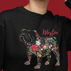 Peut inclure: Sweat-shirt noir avec un bouledogue floral et le nom "Winston" en rouge. Le bouledogue est orn&eacute; de fleurs rouges, de pommes de pin et de verdure. Un v&ecirc;tement unique et festif.