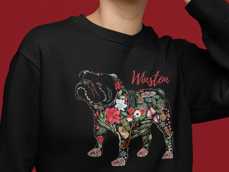 Peut inclure: Sweat-shirt noir avec un bouledogue floral et le nom "Winston" en rouge. Le bouledogue est orn&eacute; de fleurs rouges, de pommes de pin et de verdure. Un v&ecirc;tement unique et festif.