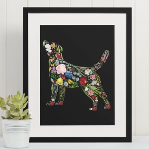 May include: A framed art print featuring a dog silhouette filled with colorful flowers and foliage against a black background. The artwork is in a black frame with a white mat, and a small succulent plant in a metal pot is in the foreground.