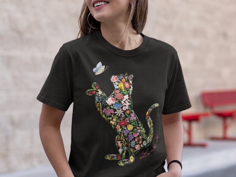 May include: Black t-shirt featuring a floral cat design with a butterfly. The cat is filled with colorful flowers and leaves. A small butterfly hovers near the cat's paw. The word "Love" is written in cursive.