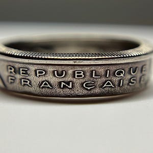 Puede incluir: Un anillo de plata hecho con una moneda francesa. El anillo tiene la inscripción "REPUBLIQUE FRANCAISE".