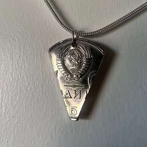 May include: A silver necklace with a triangular pendant featuring a Soviet hammer and sickle emblem and the Cyrillic text "СССР" (USSR).