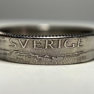 May include: A silver ring made from a Swedish coin. The ring features the word "SVERIGE" engraved on the side.