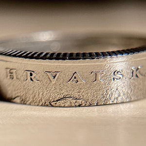 May include: A silver ring made from a coin with the inscription "HRVATS KA" on the band.