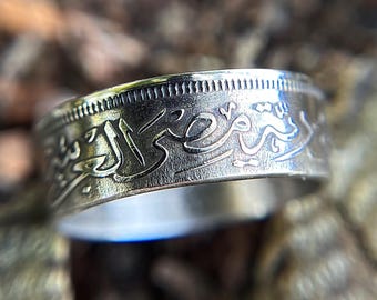 May include: A silver ring made from a coin with Arabic script engraved around the band.