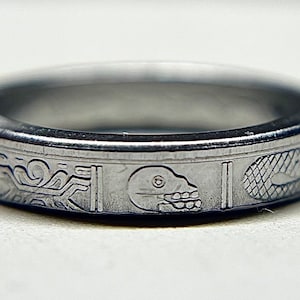 May include: A silver ring with an engraved design featuring a skull, a geometric pattern, and a stylized animal.