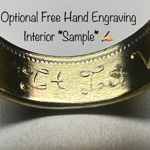 K&ouml;nnte beinhalten: Ein goldfarbener Ring mit einer glatten Innenseite, in die die kursiven Buchstaben T und S von Hand eingraviert sind. &Uuml;ber dem Ring steht der Text Optional Free Hand Engraving Interior Sample sowie ein kleines Symbol einer Hand mit Stift.