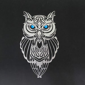 May include: A black and white stylized owl with blue eyes. The owl has intricate details and a tribal design.