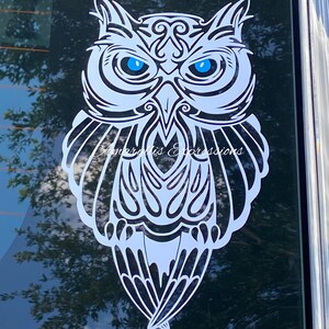 May include: White owl silhouette with intricate tribal patterns and bright blue eyes. The owl is facing forward with its wings spread out.