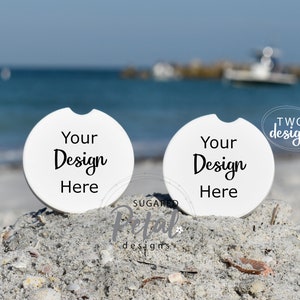 May include: Two white round beverage coasters with the text "Your Design Here" on a sandy beach with seashells. The coasters are blank and ready to be customized.