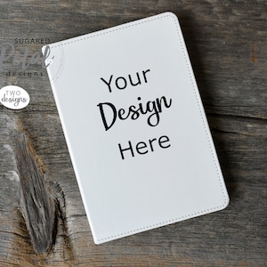 May include: White leather-bound journal with stitched edges, lying on a wooden surface. The cover has the text "Your Design Here" printed in black.