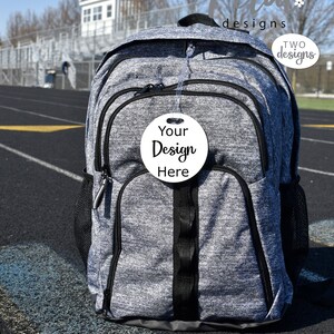 May include: Gray backpack with a black zipper and a white round tag that says "Your Design Here".