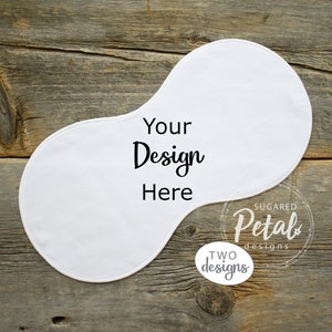 May include: White cotton baby bib with a peanut shape. The bib has the text "Your Design Here" printed on it. The bib is on a wooden background.