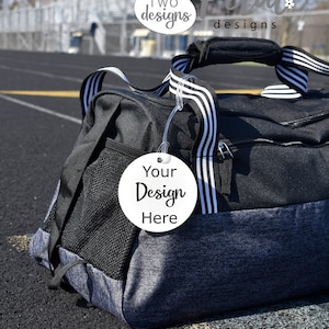 May include: A black and grey duffel bag with a white zipper and a white round tag that says "Your Design Here". The bag is sitting on a black surface. The text "TWO designs" and "SUGAR Petal designs" are visible in the background.