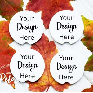 May include: Four white ceramic coasters with a cut-out for a beverage. Each coaster has the text "Your Design Here" in black cursive font. The coasters are surrounded by fall leaves in shades of red, orange, and yellow.