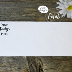 Puede incluir: Una tarjeta blanca en blanco con el texto "Your Design Here" sobre un fondo de madera. La tarjeta está rodeada por una flor blanca y dos logotipos, uno que dice "TWO designs" y el otro que dice "SUGAR Petal designs".