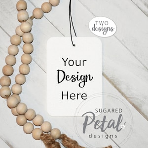 Puede incluir: Una etiqueta rectangular blanca con el texto "Your Design Here" colgando de una guirnalda de cuentas de madera marrón con un borla de yute. La etiqueta está etiquetada "Sugered Petal designs" en un círculo.