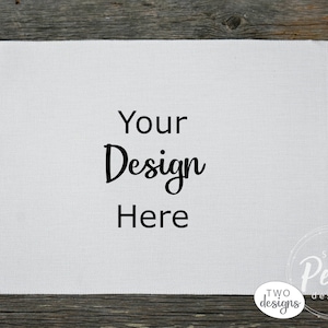Könnte beinhalten: Weißes Leinen-Geschirrtuch mit dem Text "Your Design Here" in Schwarz gedruckt. Das Handtuch liegt auf einer Holzoberfläche.