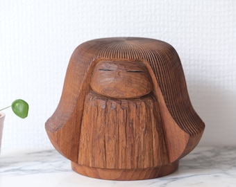 May include: A wooden sculpture of a person with a closed-eye expression. The sculpture is carved with intricate details and has a warm brown colour.