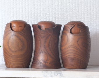 May include: Three wooden containers with lids, each with a unique carved design. The containers are made of dark brown wood with a natural grain pattern.