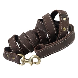 May include: A rolled-up brown leather dog leash with white stitching and brass-colored hardware. The leash has a loop handle and a metal clasp for attaching to a dog's collar. The leather appears to be suede.