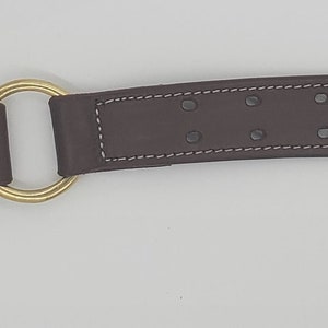 Puede incluir: Un collar de perro de cuero marr&oacute;n con una hebilla y un anillo en D de lat&oacute;n. El collar tiene un borde cosido y varias filas de agujeros para el ajuste.