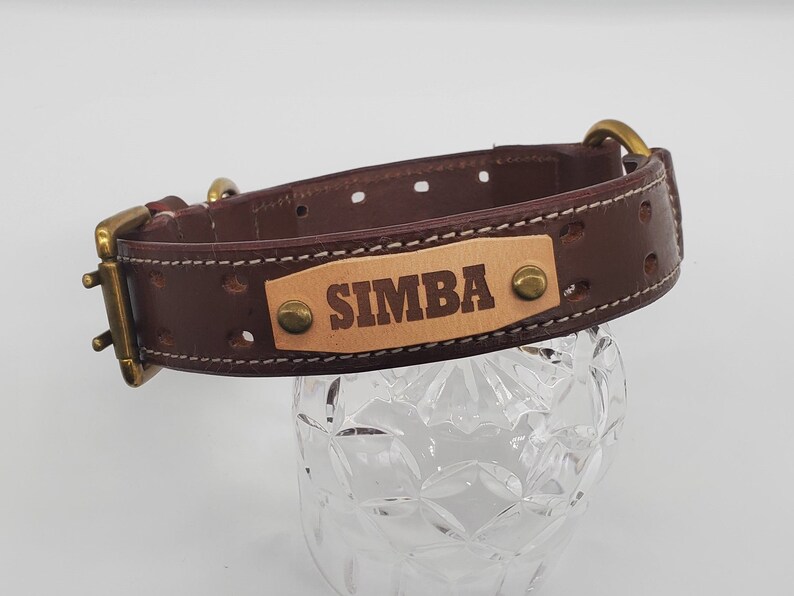 Puede incluir: Collar de perro de cuero marr&oacute;n con hebilla de lat&oacute;n y una placa de identificaci&oacute;n que dice "SIMBA".