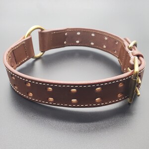 Puede incluir: Collar de perro de cuero marr&oacute;n con herrajes de lat&oacute;n y un dise&ntilde;o cosido. El collar tiene un anillo en D y una hebilla.