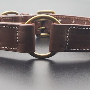 Puede incluir: Un collar de perro de cuero marr&oacute;n con costuras blancas y un anillo en D de lat&oacute;n. El collar tiene dos filas de agujeros para ajustar el tama&ntilde;o.