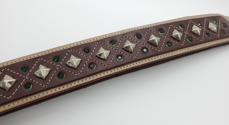 May include: Brown leather belt with a decorative design of silver pyramid studs and green rhinestones.