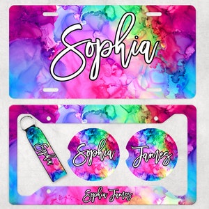 May include: A colorful set of personalized car accessories featuring a license plate frame, two coasters, and a key chain. The design features a vibrant abstract watercolor background with the names "Sophia" and "James" in a handwritten font.