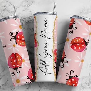 May include: Three stainless steel tumblers with lids. The tumblers are pink with a white daisy and ladybug pattern. The middle tumbler has the text "Add Your Name" in black script.