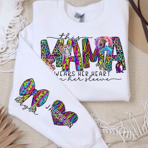 May include: White sweatshirt with the text "this mama wears her heart on her sleeve" in colorful letters with animal print designs. The sweatshirt has two colorful patches on the sleeves, one with a bow and the name "Kaylee" and the other with a heart and the name "Jackson".