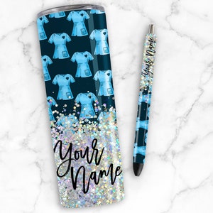 Puede incluir: Un vaso azul y blanco con acabado brillante y un patr&oacute;n de batas azules con un coraz&oacute;n en el bolsillo. El vaso tiene el texto "Your Name" en la parte inferior. Tambi&eacute;n se muestra un bol&iacute;grafo a juego con el mismo patr&oacute;n y texto.