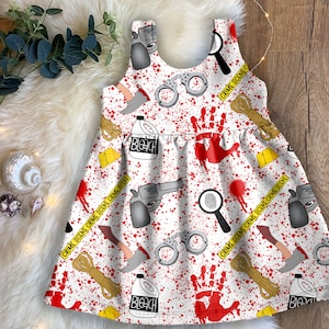 K&ouml;nnte beinhalten: Wei&szlig;es, &auml;rmelloses Kleid mit einem roten und wei&szlig;en Tatort-Druck. Der Druck enth&auml;lt Handabdr&uuml;cke, Handschellen, Bleichmittelflaschen, eine Waffe und Absperrband. Der Text auf dem Band lautet "CRIME SCENE CRIME SCENE CRIME SCENE".
