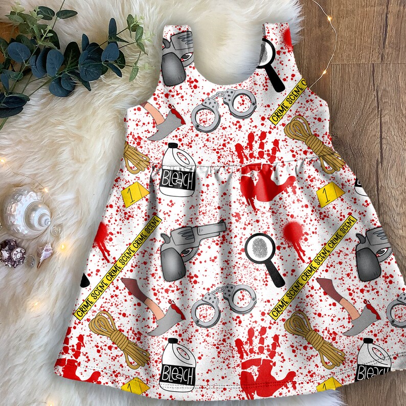 K&ouml;nnte beinhalten: Wei&szlig;es, &auml;rmelloses Kleid mit einem roten und wei&szlig;en Tatort-Druck. Der Druck enth&auml;lt Handabdr&uuml;cke, Handschellen, Bleichmittelflaschen, eine Waffe und Absperrband. Der Text auf dem Band lautet "CRIME SCENE CRIME SCENE CRIME SCENE".