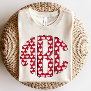 May include: A white t-shirt with a red and white monogram design featuring the letters "ABC" in a heart pattern.