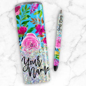 Puede incluir: Un vaso de acero inoxidable con fondo azul y dise&ntilde;o floral. El vaso est&aacute; lleno de purpurina plateada y las palabras "Your Name" est&aacute;n escritas en negro. Tambi&eacute;n se incluye un bol&iacute;grafo a juego con el mismo dise&ntilde;o.