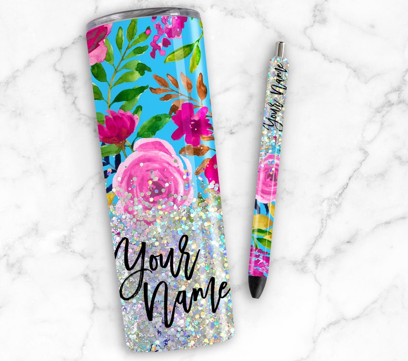 Puede incluir: Un vaso de acero inoxidable con fondo azul y dise&ntilde;o floral. El vaso est&aacute; lleno de purpurina plateada y las palabras "Your Name" est&aacute;n escritas en negro. Tambi&eacute;n se incluye un bol&iacute;grafo a juego con el mismo dise&ntilde;o.