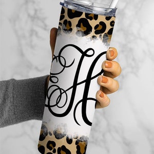 Puede incluir: Un vaso de acero inoxidable con fondo blanco y dise&ntilde;o de estampado de leopardo. El vaso tiene una letra "H" negra en cursiva en la parte delantera.