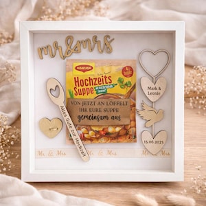 Puede incluir: Una caja de regalo de boda enmarcada en blanco con detalles de madera. La caja incluye un paquete de sopa Maggi, corazones de madera, una paloma y una cuchara. El texto "mr & mrs" y "Alles Gute zur Hochzeit" son visibles. También se muestra la fecha 15.06.2025.