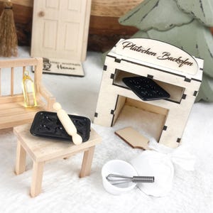 Puede incluir: Un juego de cocina de juguete de madera en miniatura con un horno pequeño, una mesa, un rodillo, una bandeja para hornear y un tazón con un batidor. El horno tiene un letrero que dice "Plätzchen Backofen".